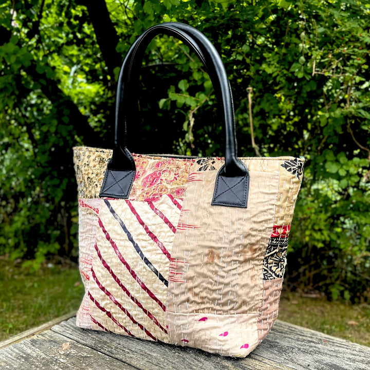 A kantha stitched patchwork cotton purse sitting on a wooden table in front of some greenery. 