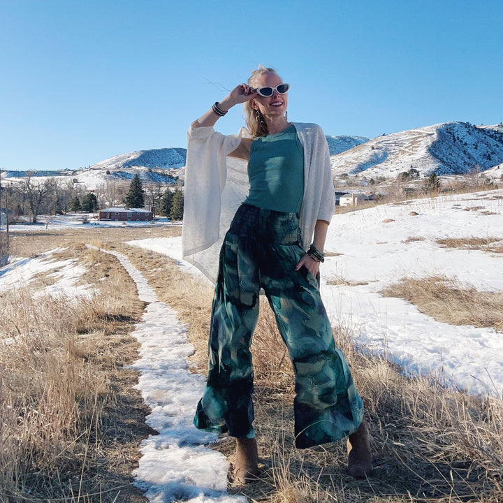 Woman in a bohemian outfit posing on a snowy path with mountains behind.