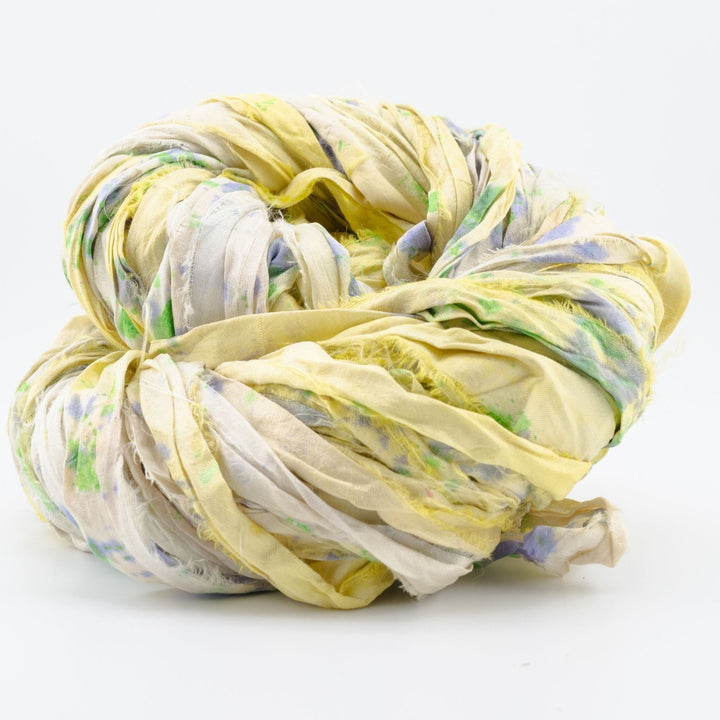 Close-up image of a skein of small batch sari silk ribbon yarn, showcasing a blend of soft yellow and green hues. The ribbon displays the distinctive, textured appearance of upcycled sari silk. Ideal for use in knitting, crocheting, weaving, and mixed media projects.