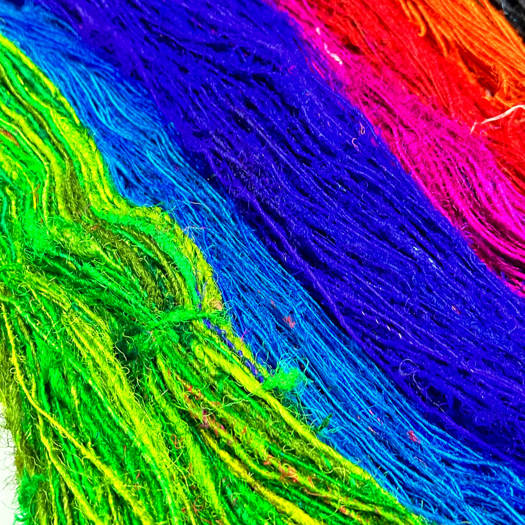 Bright rainbow-colored yarn strands laid out in green, blue, purple, red, and pink.