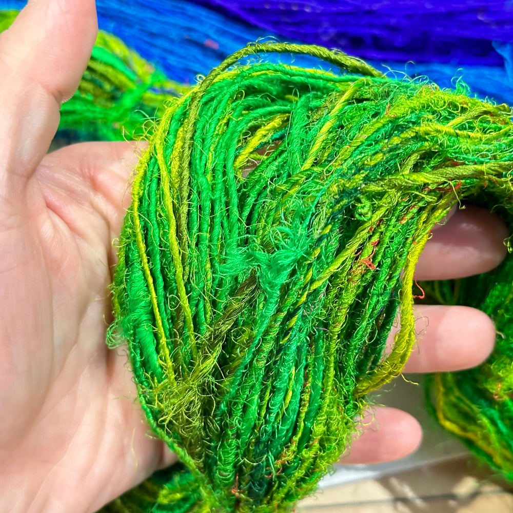 A hand holding vibrant green yarn with fibers twisted and looped.