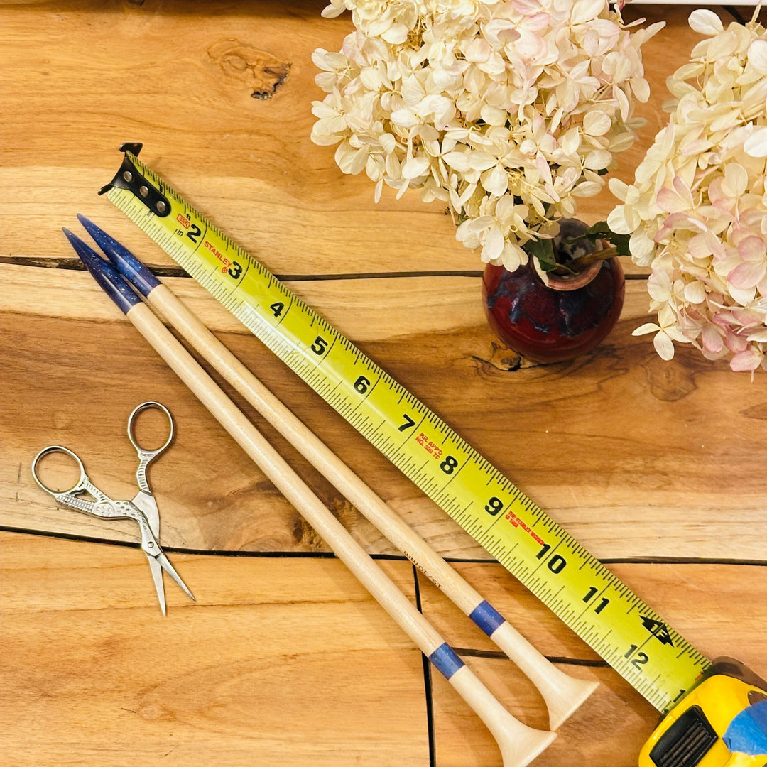 Wooden knitting needles, scissors, tape measure, and flowers on a table.