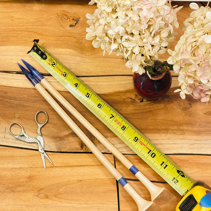 Wooden knitting needles, scissors, tape measure, and flowers on a table.