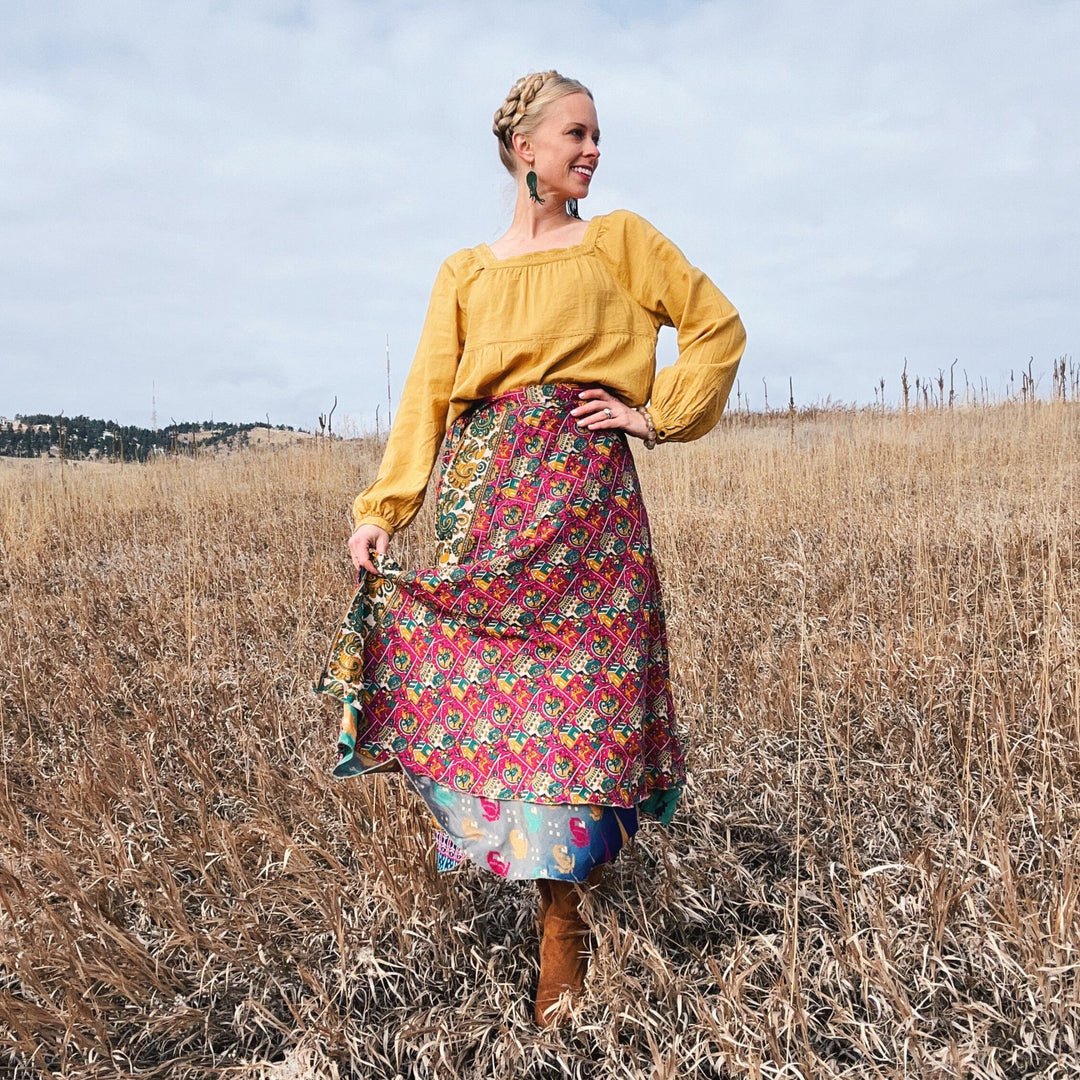 A woman in a colorful skirt posing in a dry field under a cloudy sky.