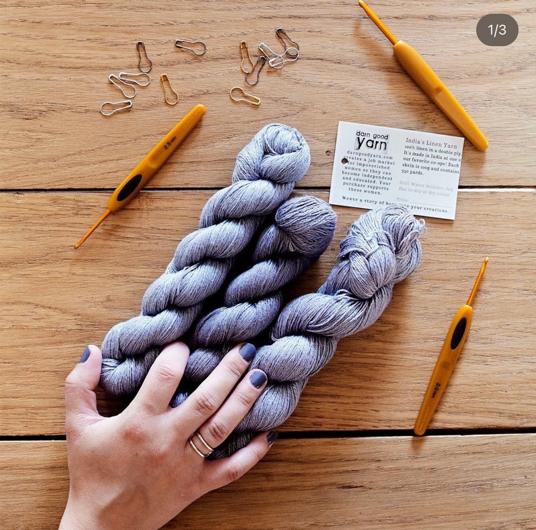 A hands holding light purple yarn skeins with crochet tools and safety pins