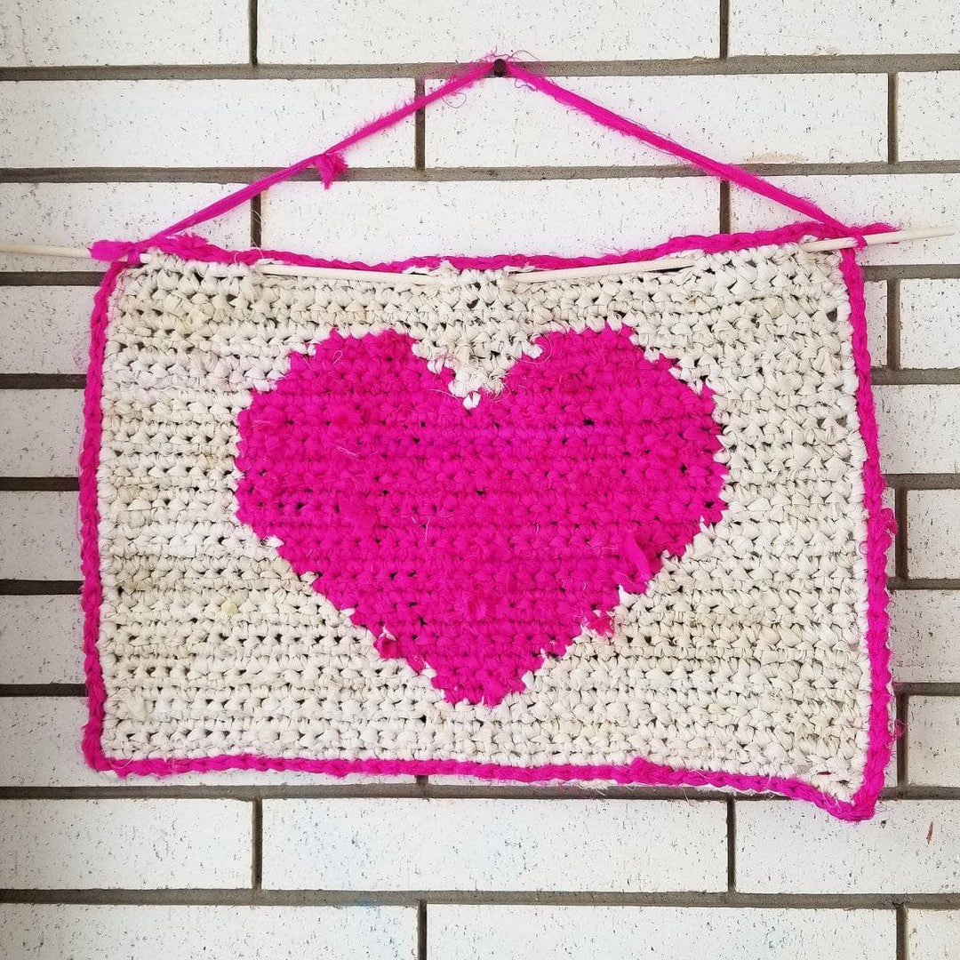 All My Love crochet Wall Hanging with hot pink heart hanging from a brick wall