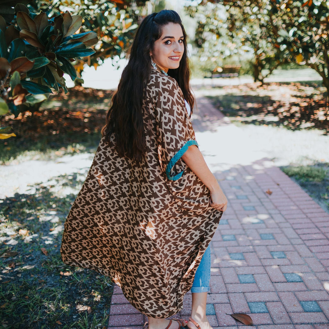 Woman in a long patterned kimono outdoors, smiling and looking back on a sunny path