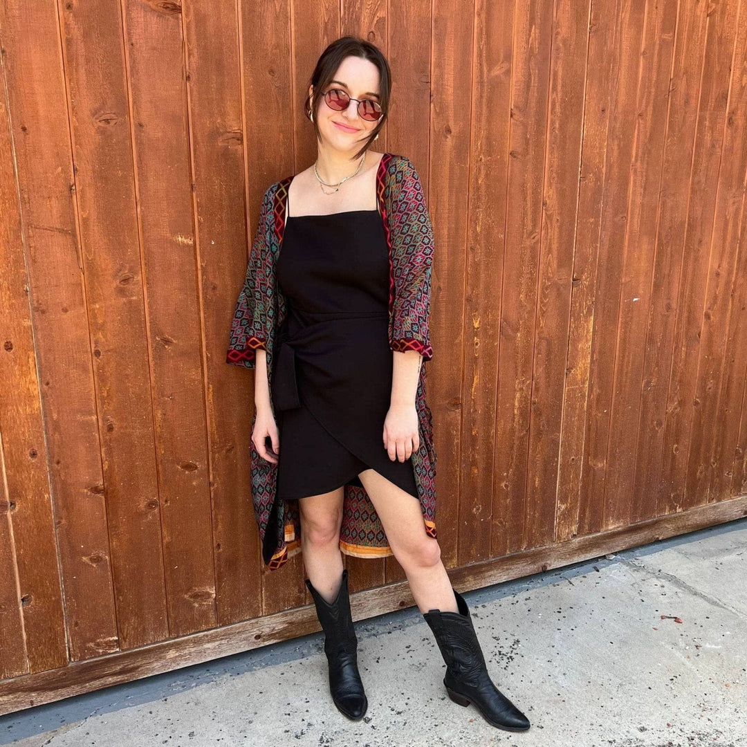 A woman standing outside wearing a black strapless dress with a black and maroon zig zag pattern sari duster overtop.