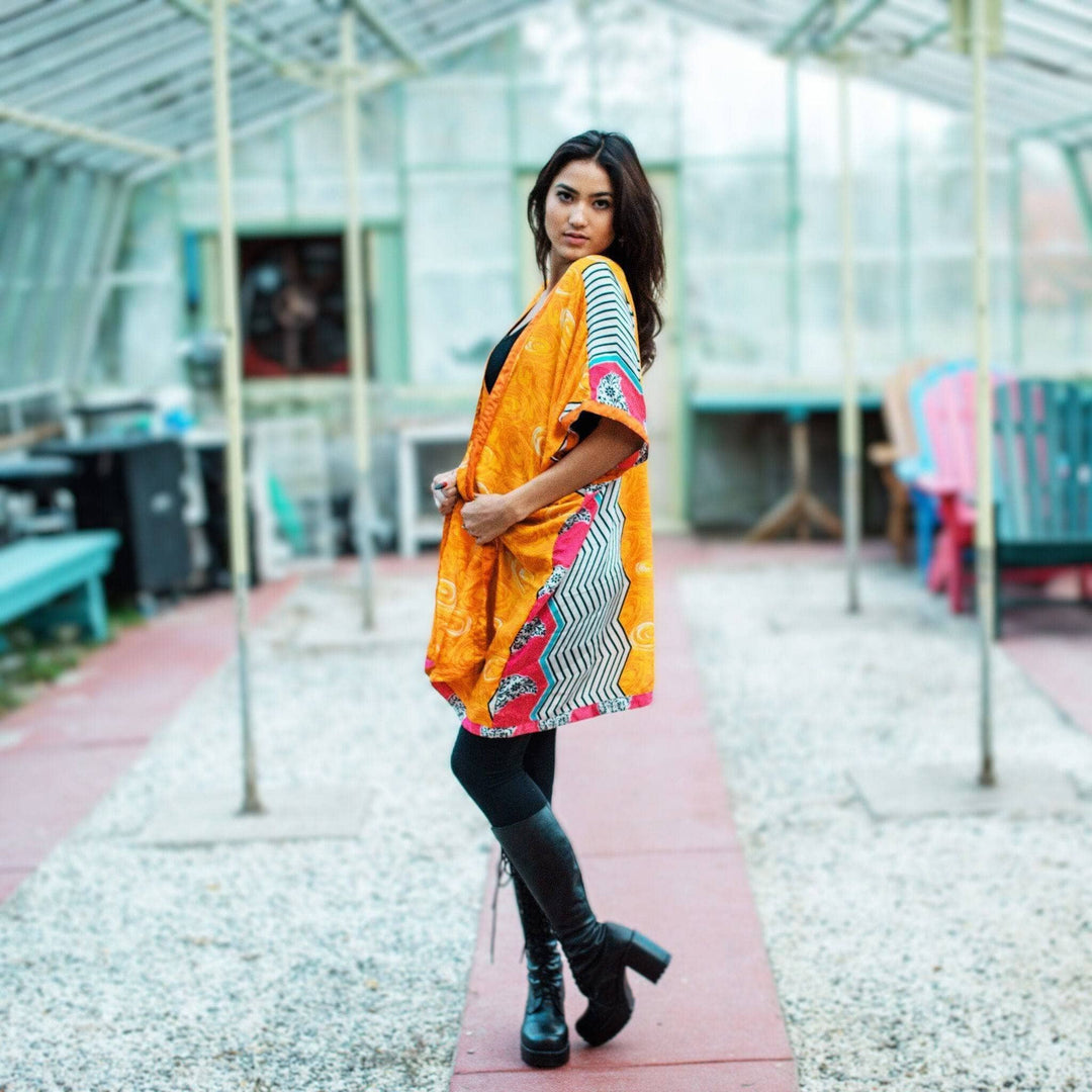 Woman in a bright orange kimono posing stylishly in a greenhouse.