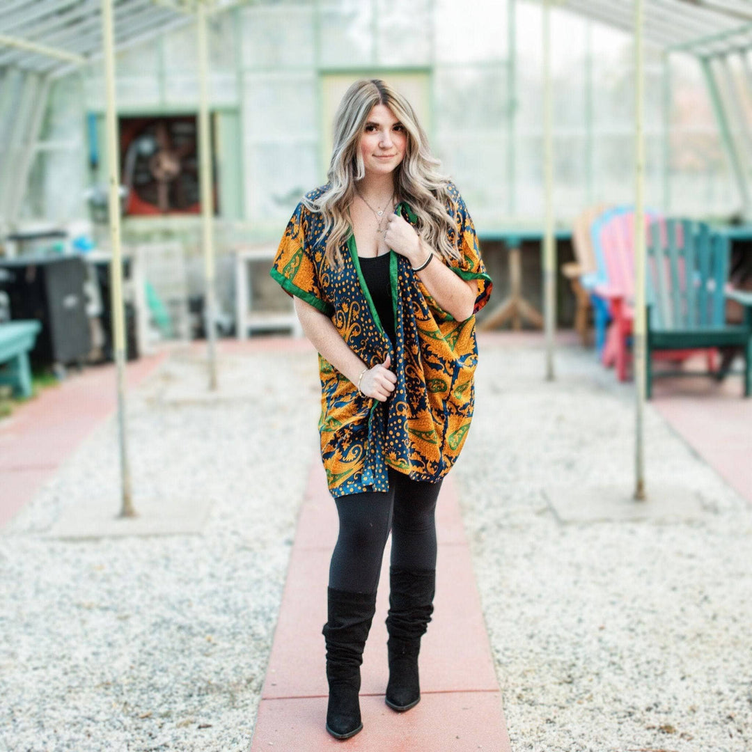 Girl wearing the amara duster standing in a greenhouse with adirondack chairs of every color in the background.