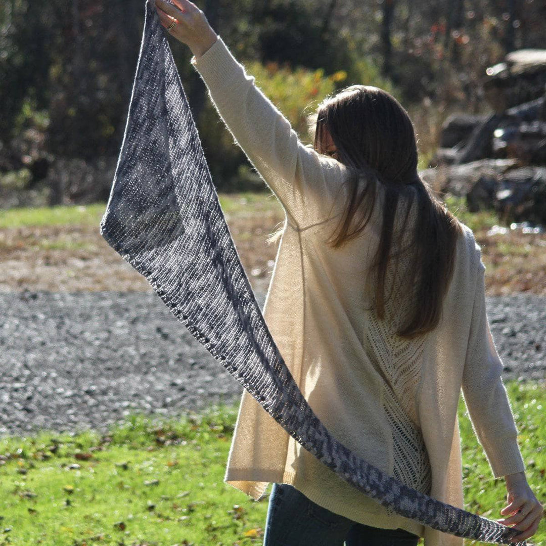 Woman holding a Andina Scarf in Date Night (grays) behind her back in front of grassy area