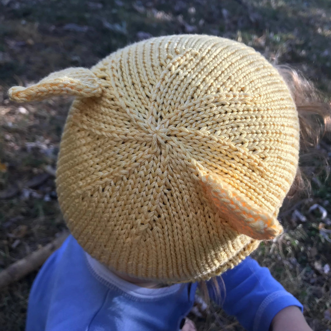 Child walking outside wearing a yellow cat ear beanie and wearing a purple shit