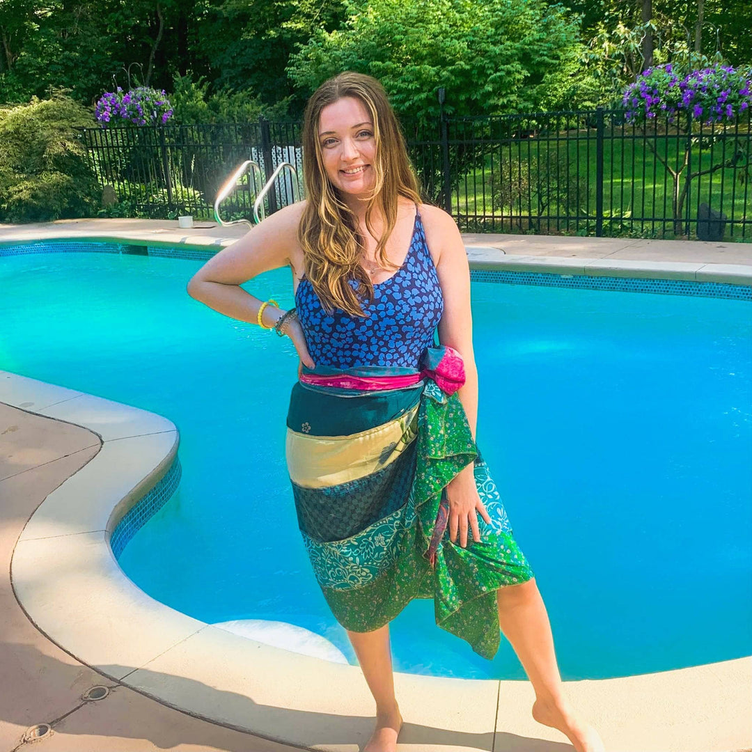 Model is wearing a blue and green Bali Breeze wrap as a beach coverup in front of a pool.