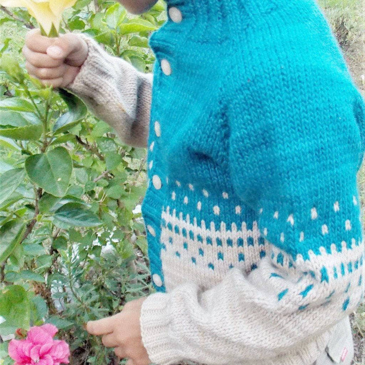 Close up view of child wearing Benja's Jacket knit sweater in blue and white and walking in a grassy area