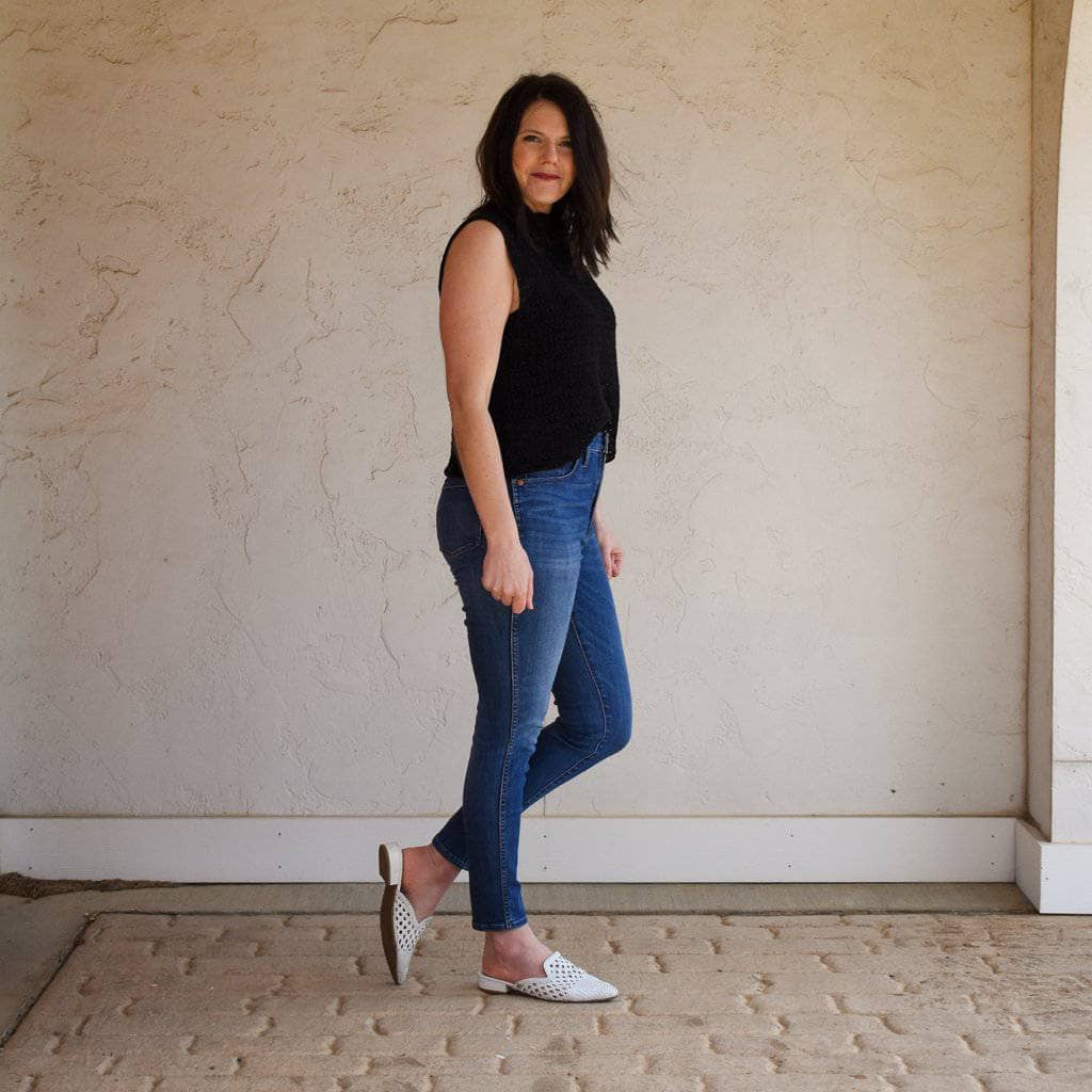 Women wearing a black crochet top outside with an off-white wall behind her