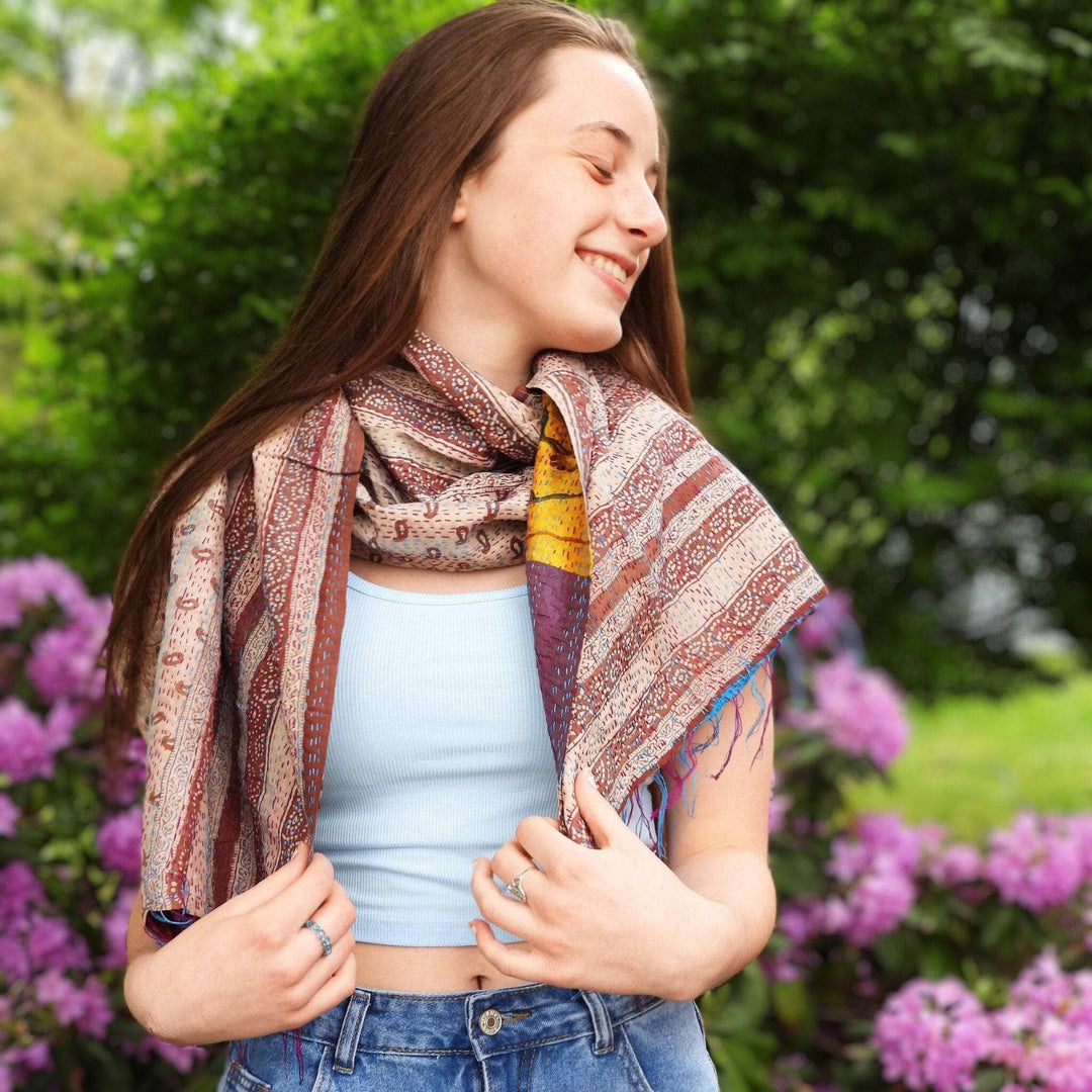 Model wearing one of a kind kantha scarf outside in front of pink flowers and greenery.