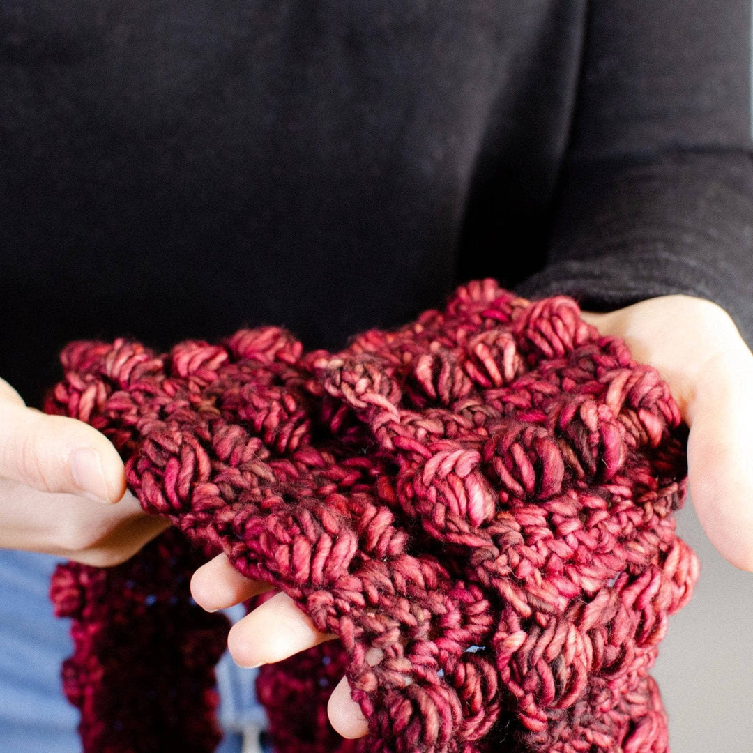 Person wearing a black shirt and jeans hold a red infinity scarf