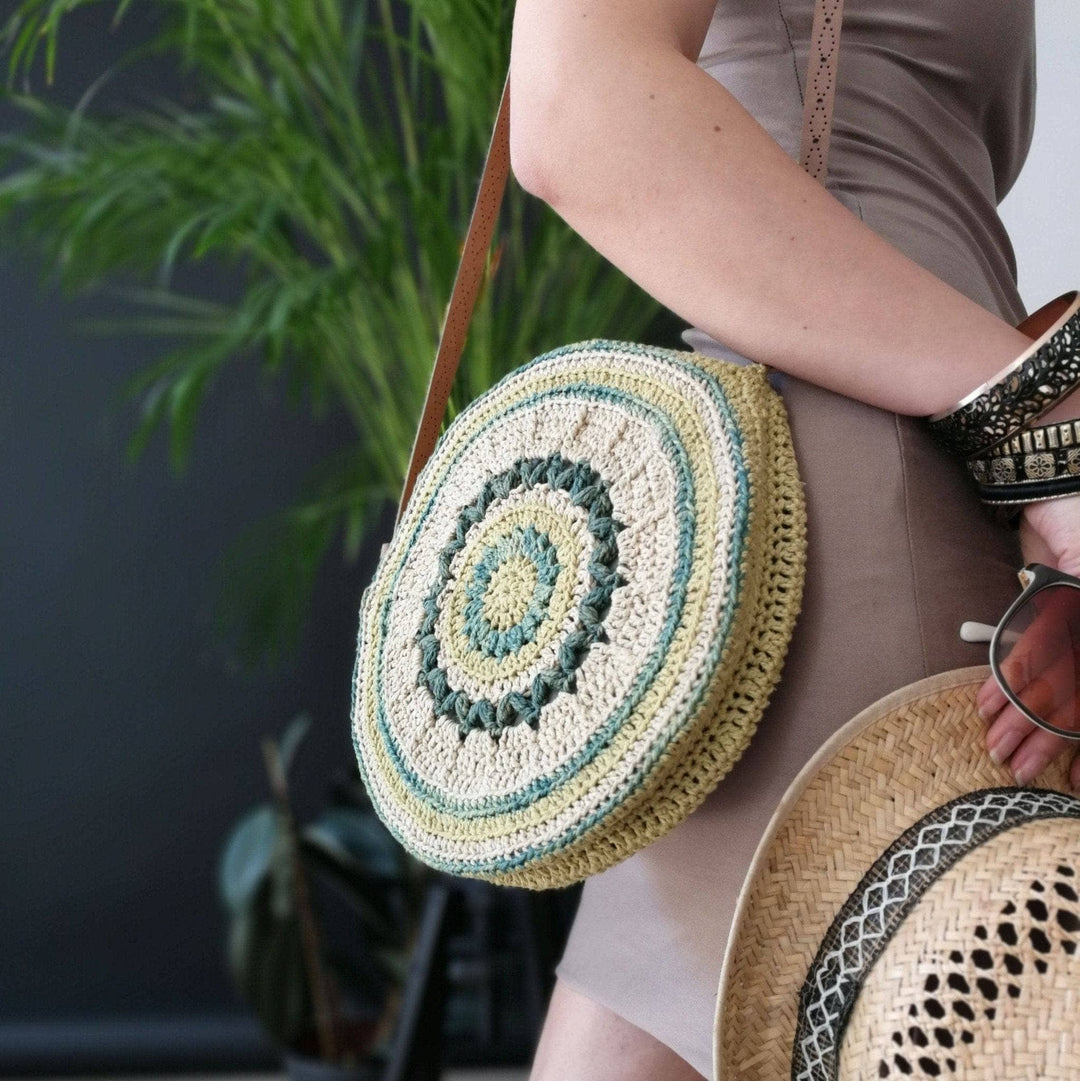 Woman wearing beige dress, circle banjo bag, straw fedora, and standing against a black wall