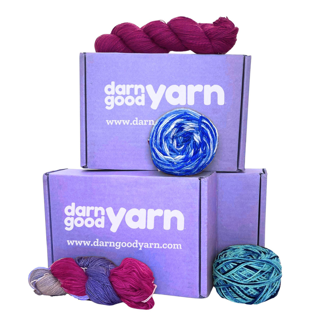 A stacked "Darn Good Yarn" purple boxes with colorful yarn skeins on top and around them