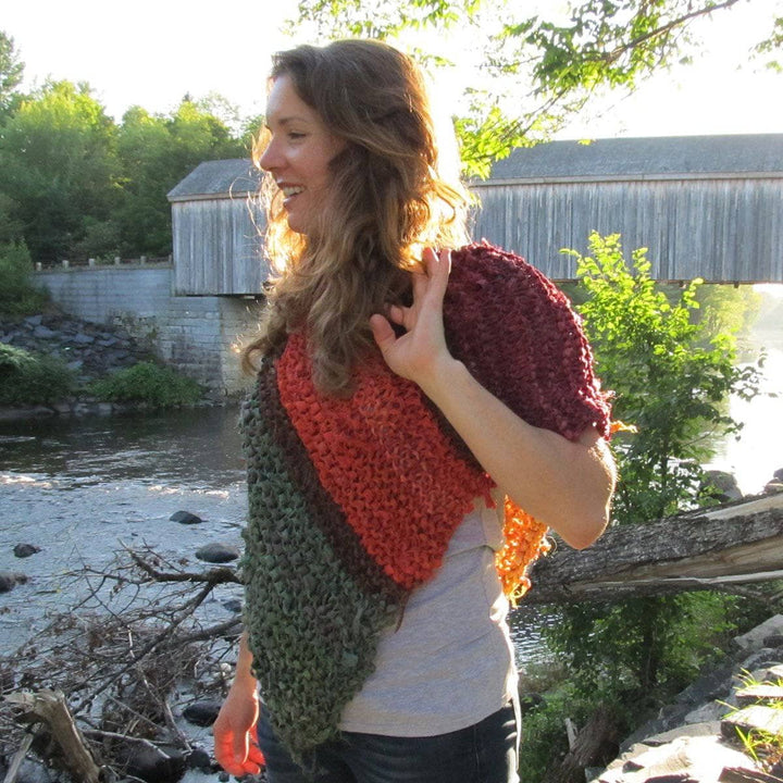 Woman wearing a red, orange, and green poncho and standing in front of a body of water