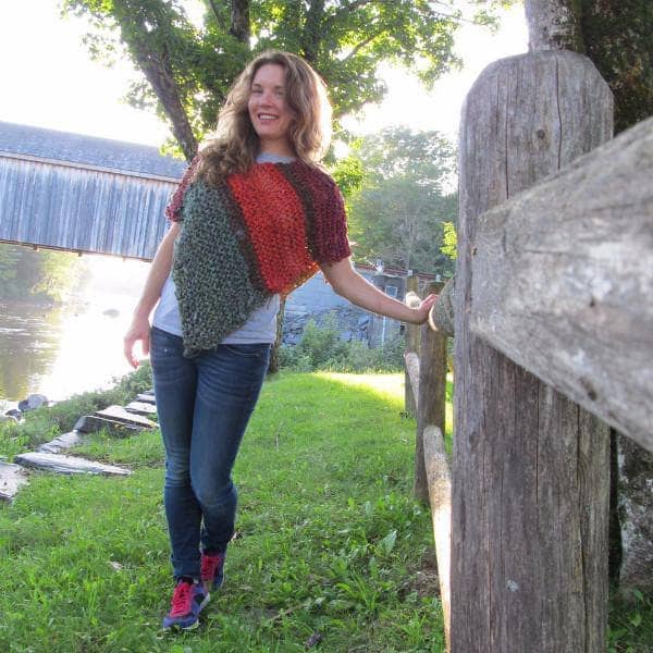 Woman wearing a red, orange, and green poncho and standing in front of a body of water