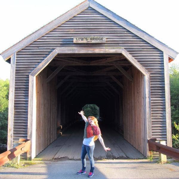 Woman wearing a red, orange, and green poncho and standing in front of a brown barn