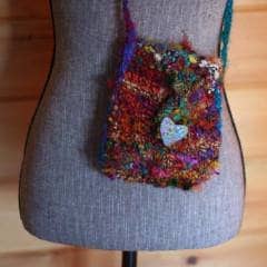 Gray mannequin wearing a multicolor mini knit purse standing in front of a wooden background