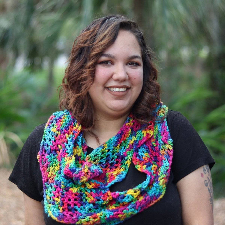 Woman wearing black tee shirt and multicolored crochet scarf and standing in front of greenery