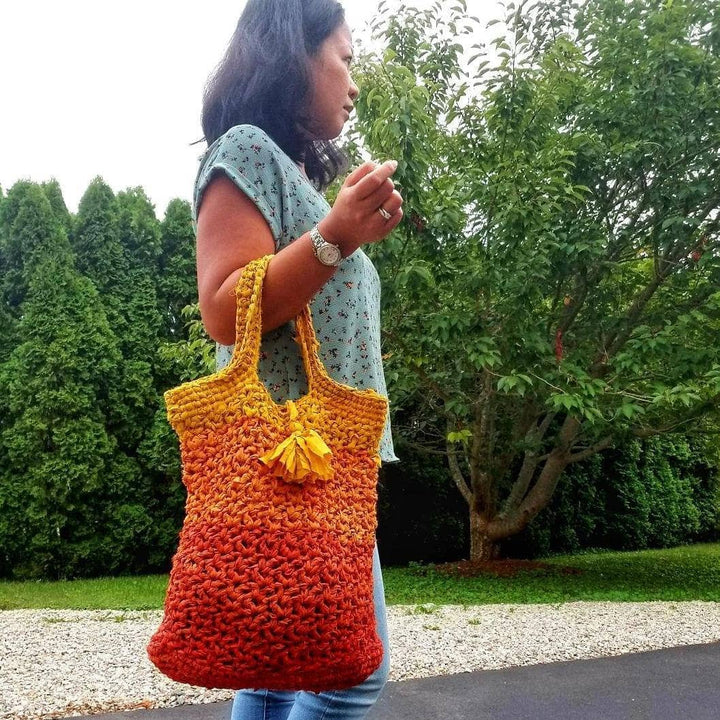 A woman holding a orange ombre tote bag outside 