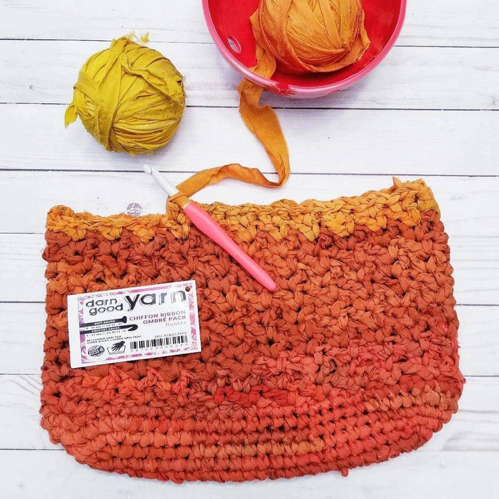 Orange tote bag on a white wooden background with a yarn bowl and chiffon ribbon