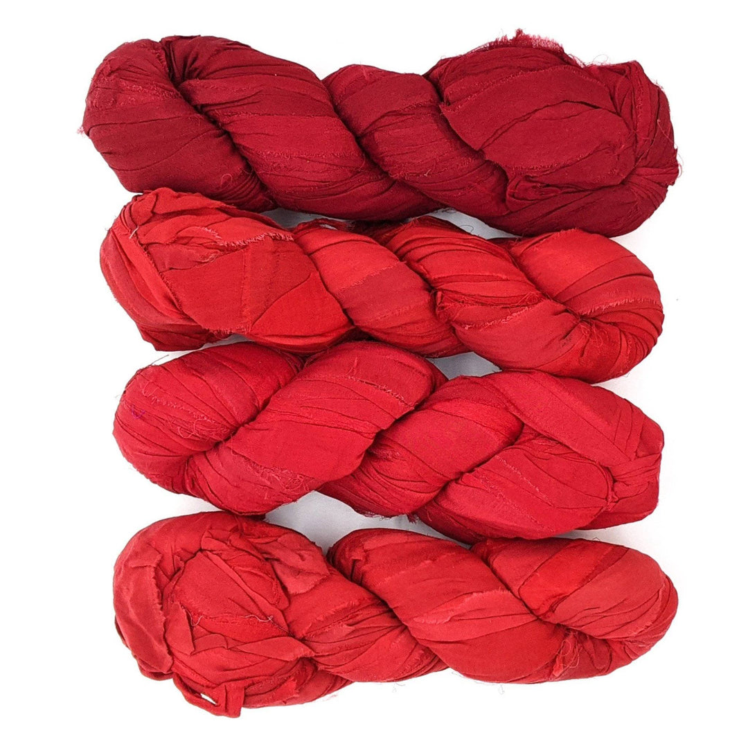 4 skeins of red ombre ribbon yarn on a white background