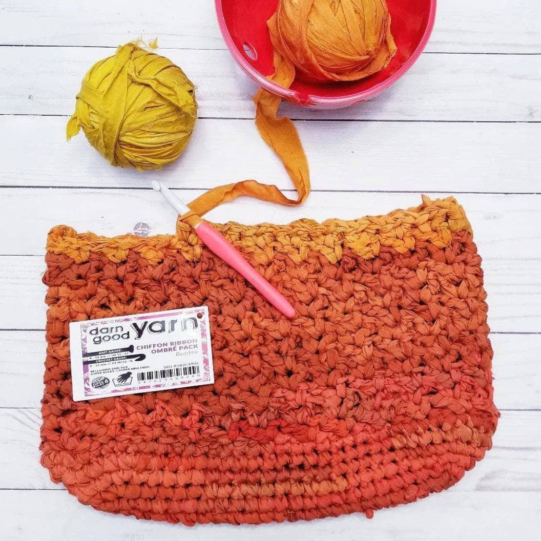 Orange tote bag on a white wooden background with a yarn bowl and chiffon ribbon