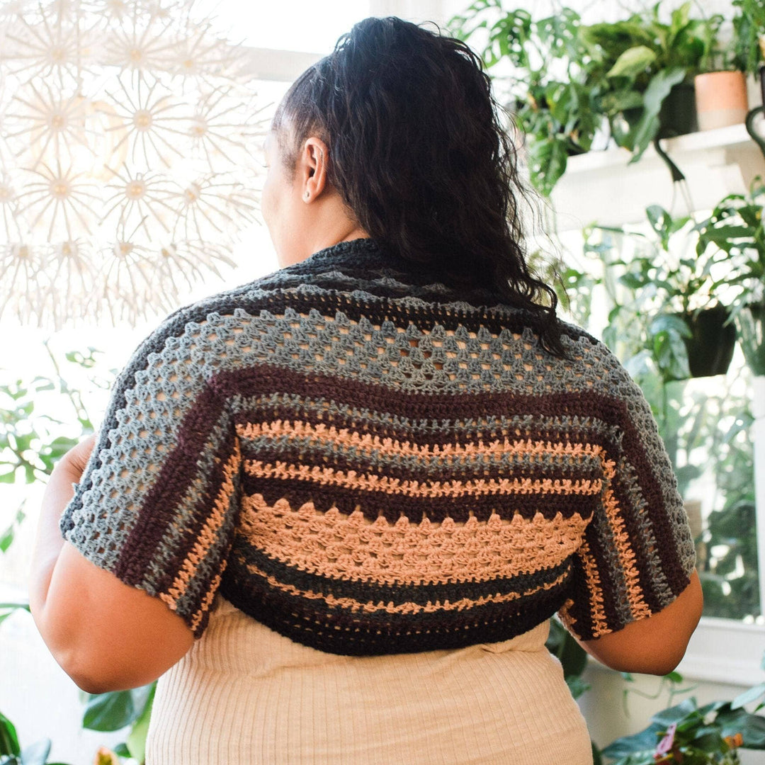 Back view of model wearing ebb and flow shrug in winter frost with potted greenery in the background.