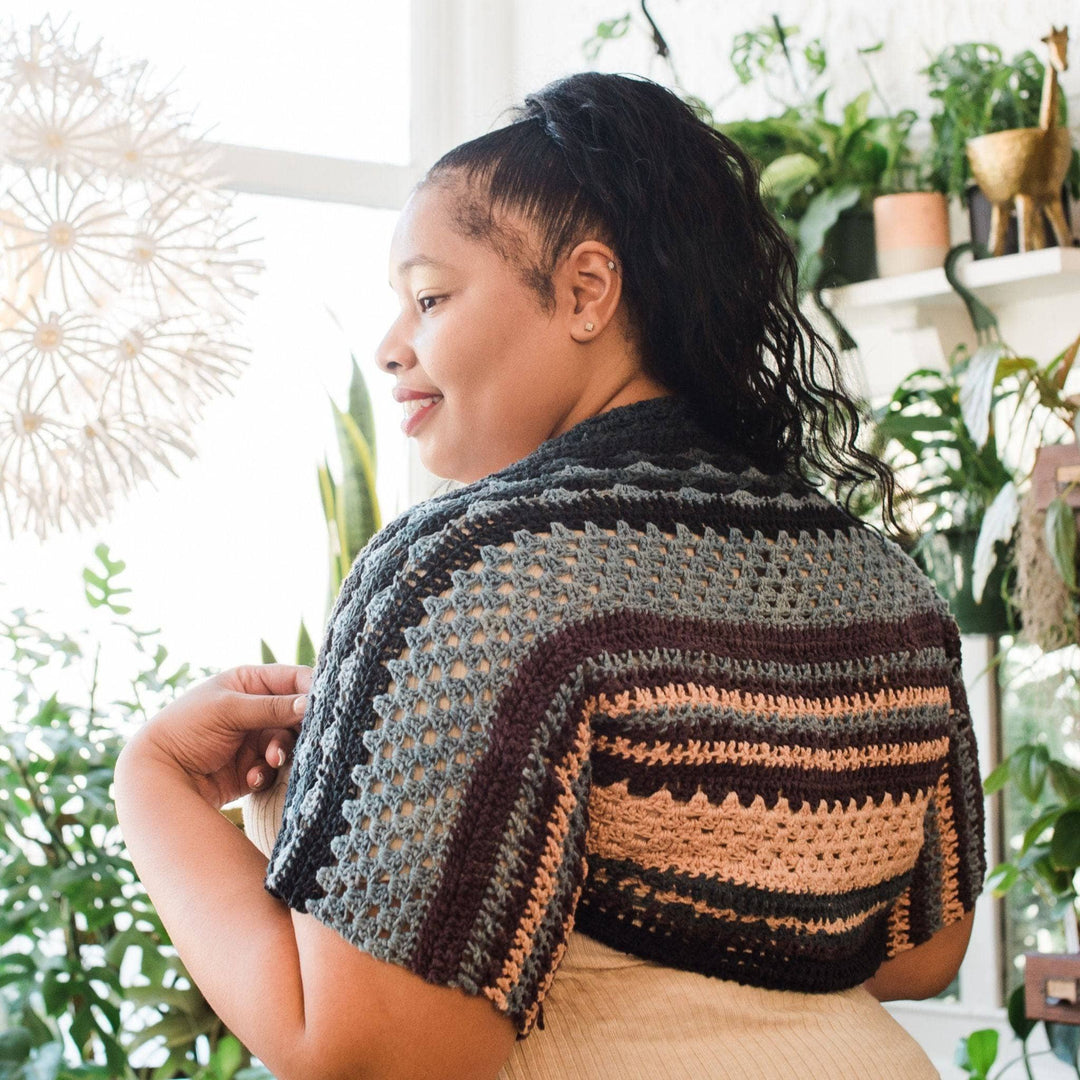 Model wearing ebb and flow shrug in winter frost with potted greenery in the background.