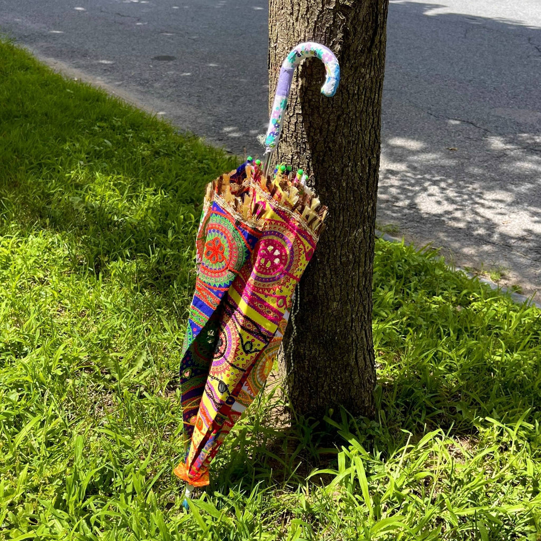 Embellished Parasol Umbrella folded up leaning against a tree, 