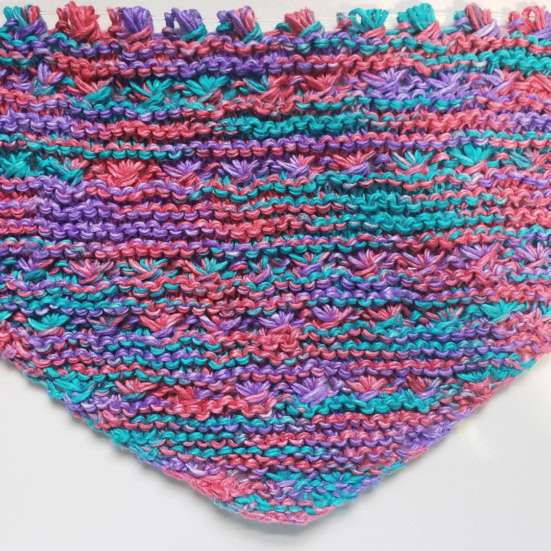 A pink, teal and blue shawl laying flat on a white background