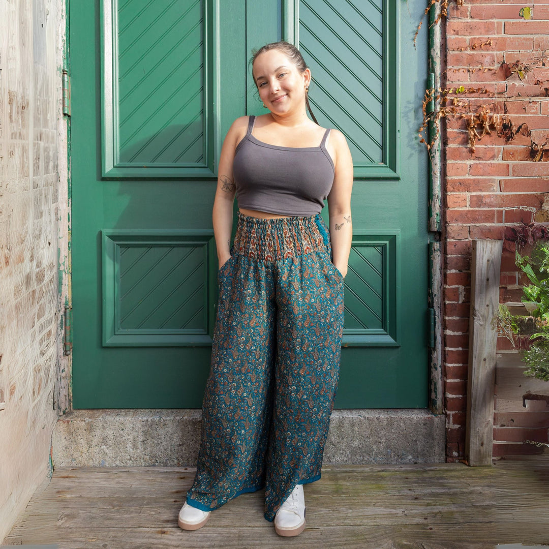 A woman in a tank top and patterned pants standing in front of a green door, hands in pockets