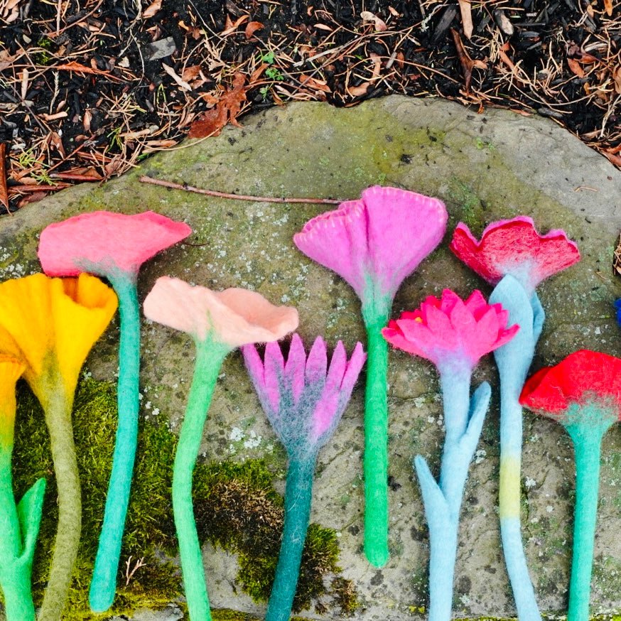 Vibrant felted flowers displayed outdoors on stone and grass.