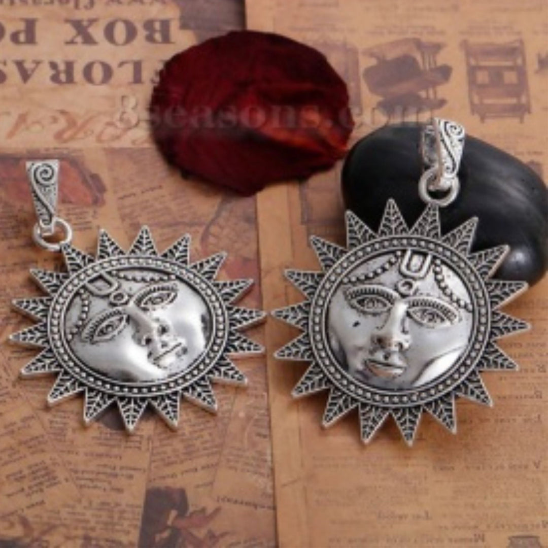 Two antique silver pendants of suns with faces sitting on a wooden background.