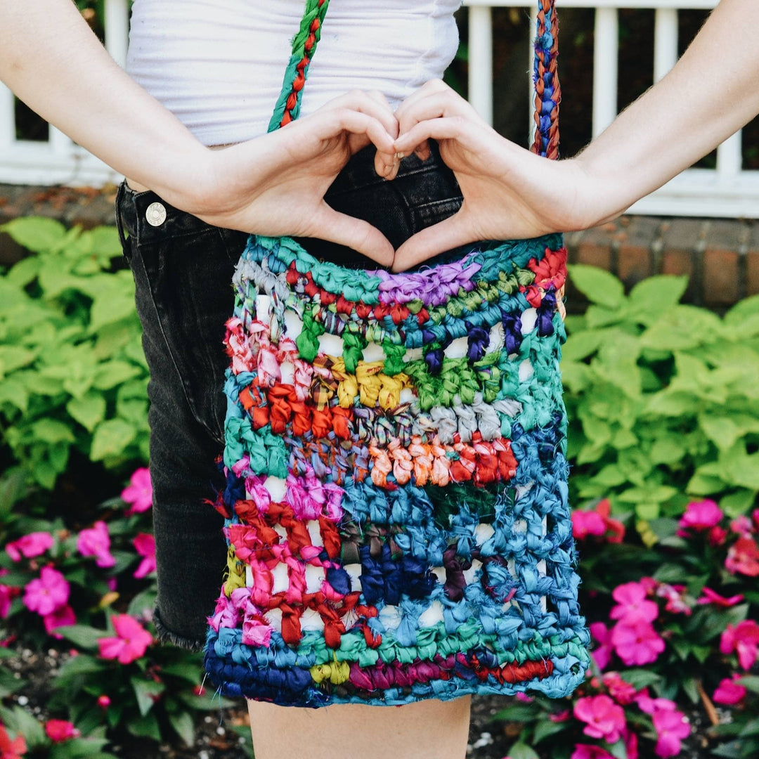 Model wearing hidden heart crochet bag closeup detail shot with greenery in the background.