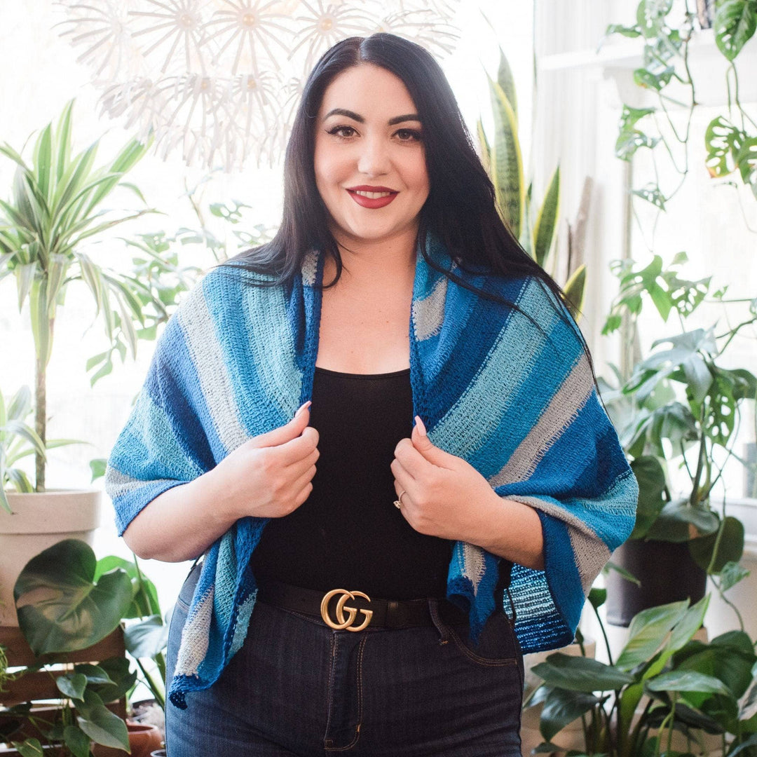 Model wearing I'm feeling plucky tunisian crochet shawl in blue with potted greenery in the background.