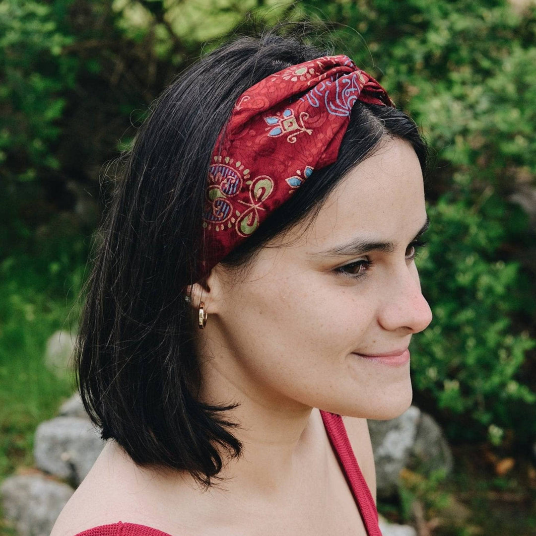 Model is wearing a sari silk kameela knot headband in maroon. The headband has mandala symbols on it in gold and blue.