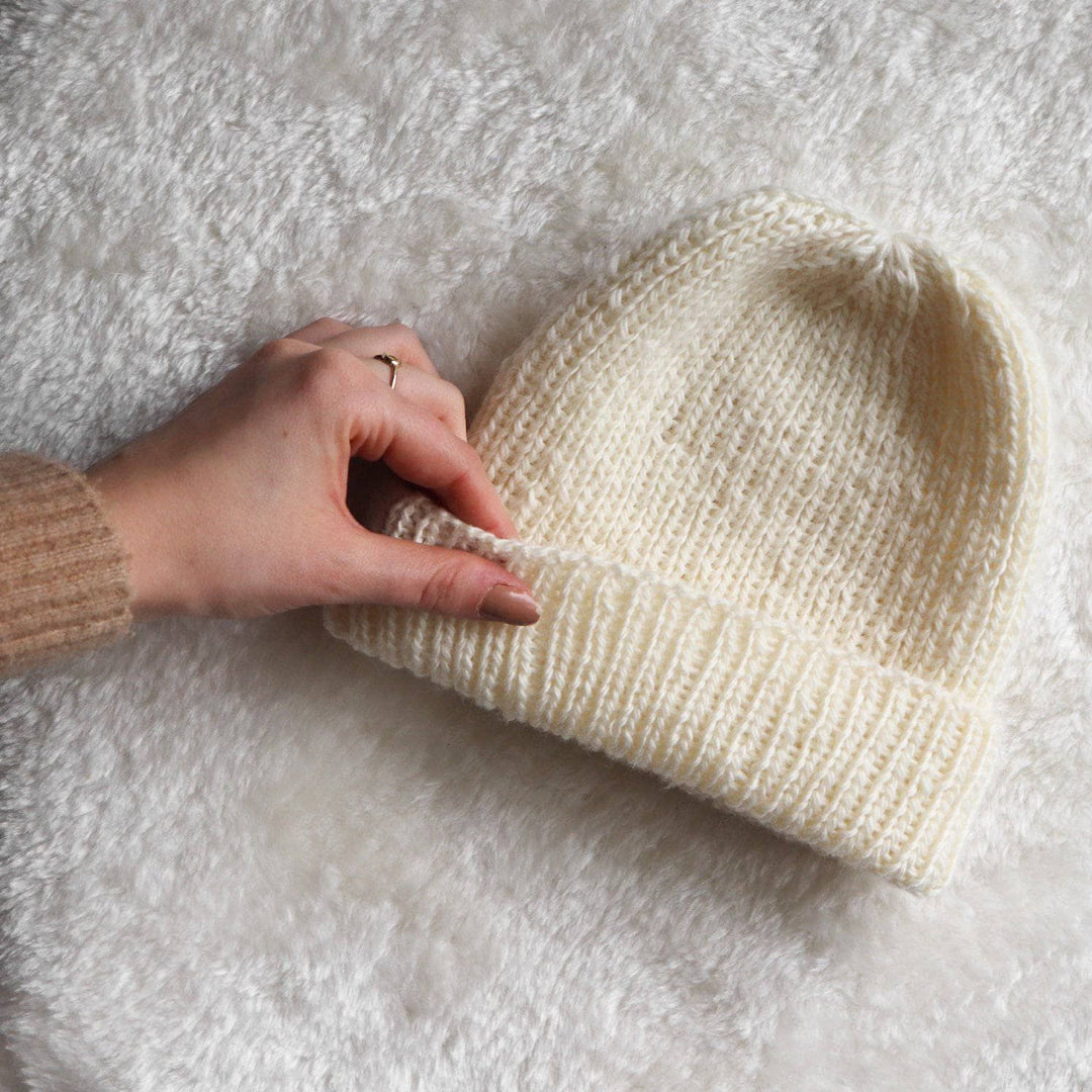 A person holding a white knit hat on a white rug