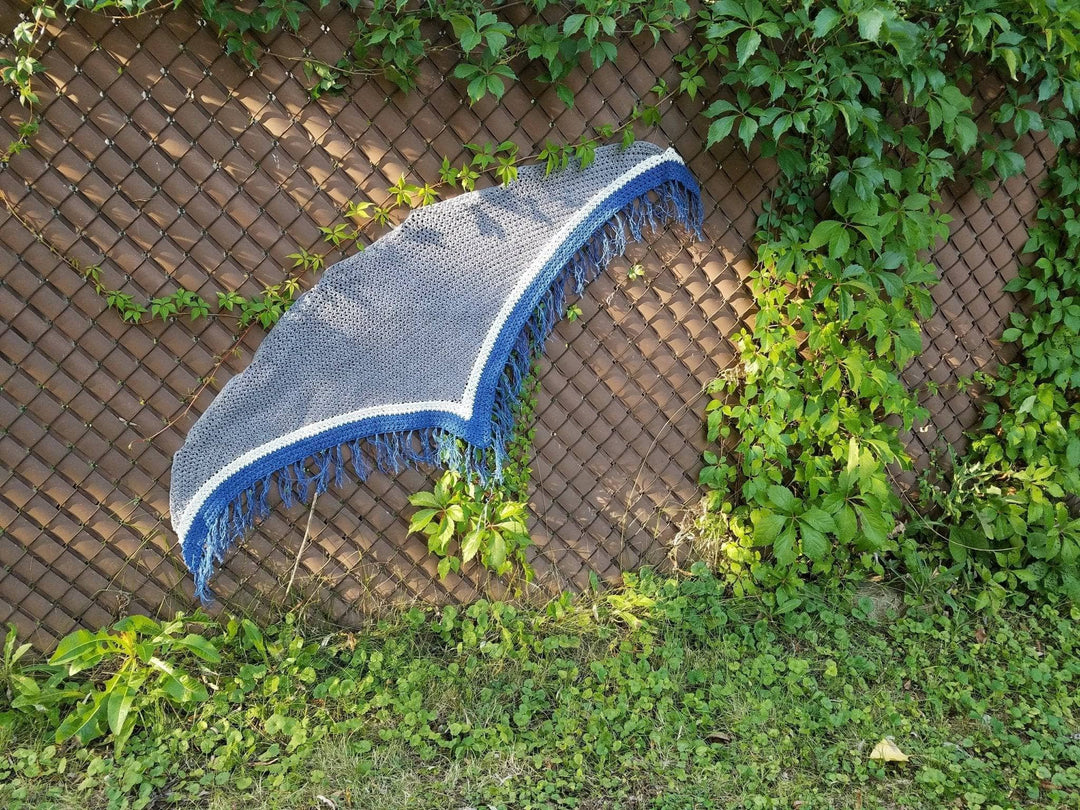 Stingray shawl hung to display shape over grass  and other greenery outdoors.