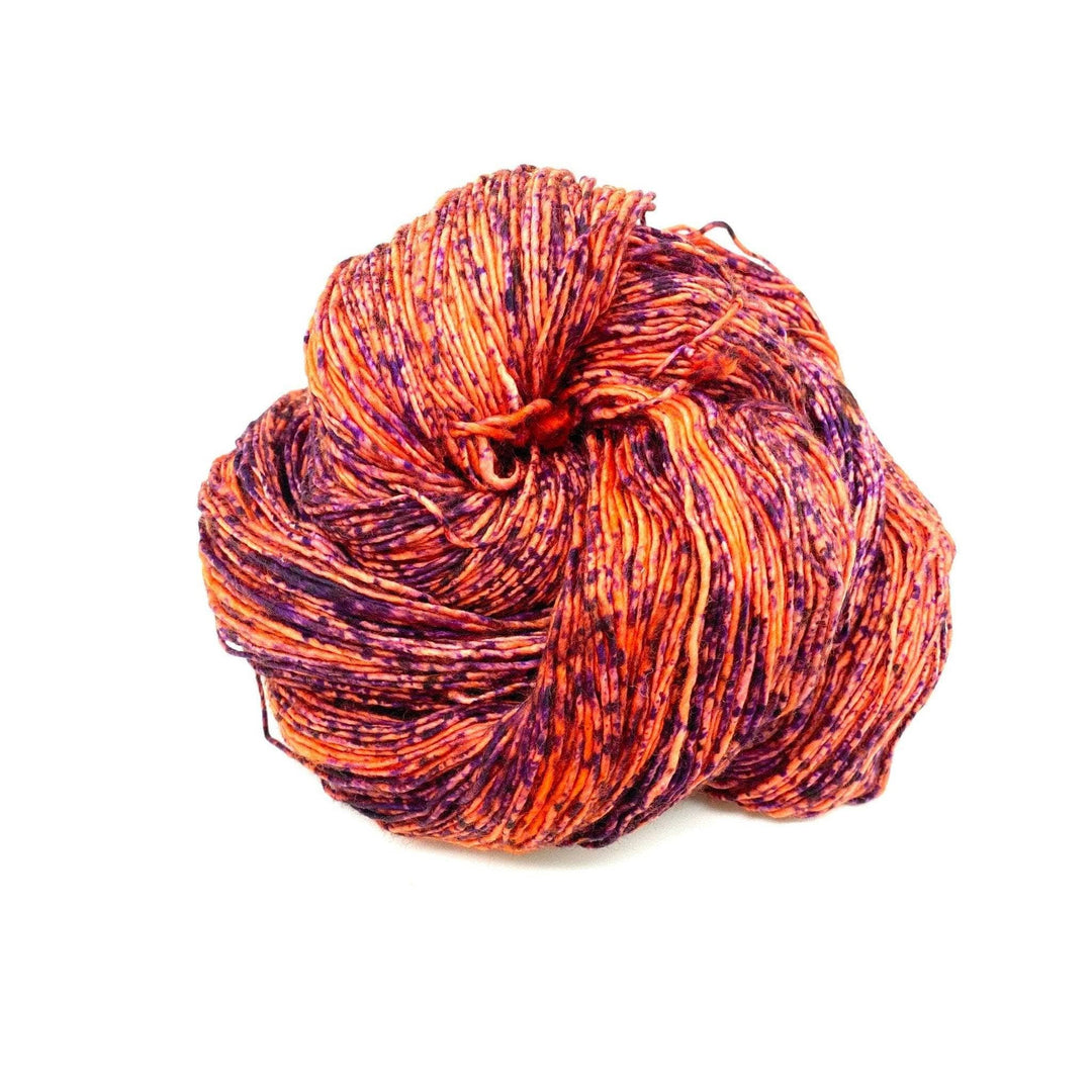 Skein of orange yarn with purple speckles in front of a white background. 