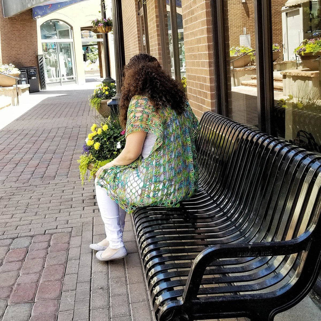 woman wearing a green poncho sitting down in a chair in a street