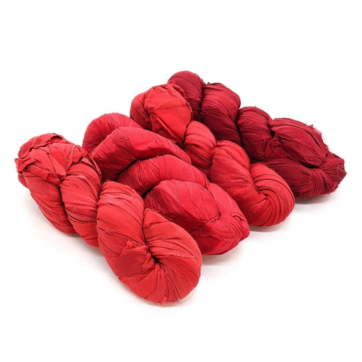 4 skeins of red ombre ribbon yarn on a white background