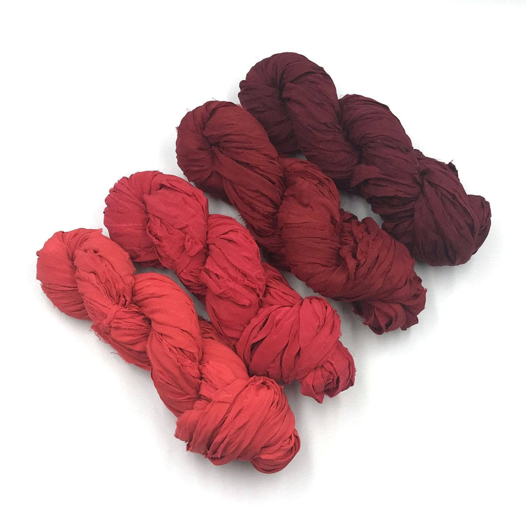 4 skeins of red ombre ribbon yarn on a white background