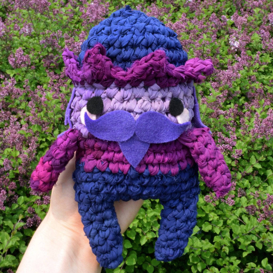 Purple amigurumi nutcracker made of silk chiffon being held by someone outside 