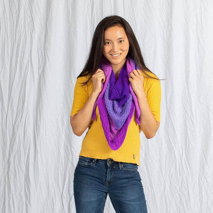 Model wearing ombre stitch sampler shawl in purple around their neck in front of a white background. 